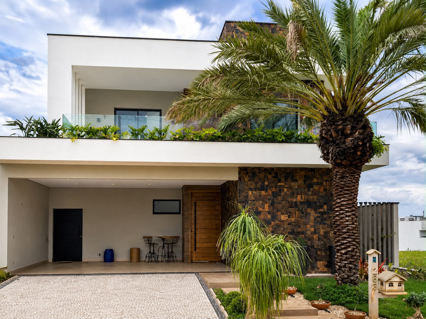Fachada de residência com guarda-corpo de vidro no terraço, porta pivotante amadeirada e palmeira
