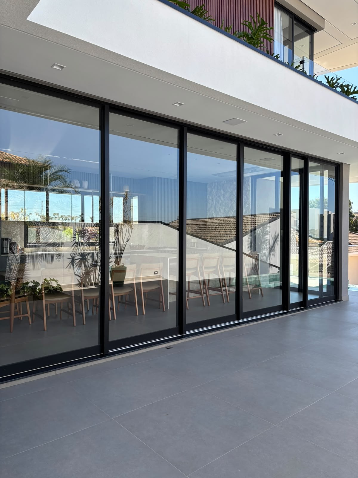 Painel de portas de correr em alumínio preto fechando a varanda gourmet, com a sala de jantar ao fundo